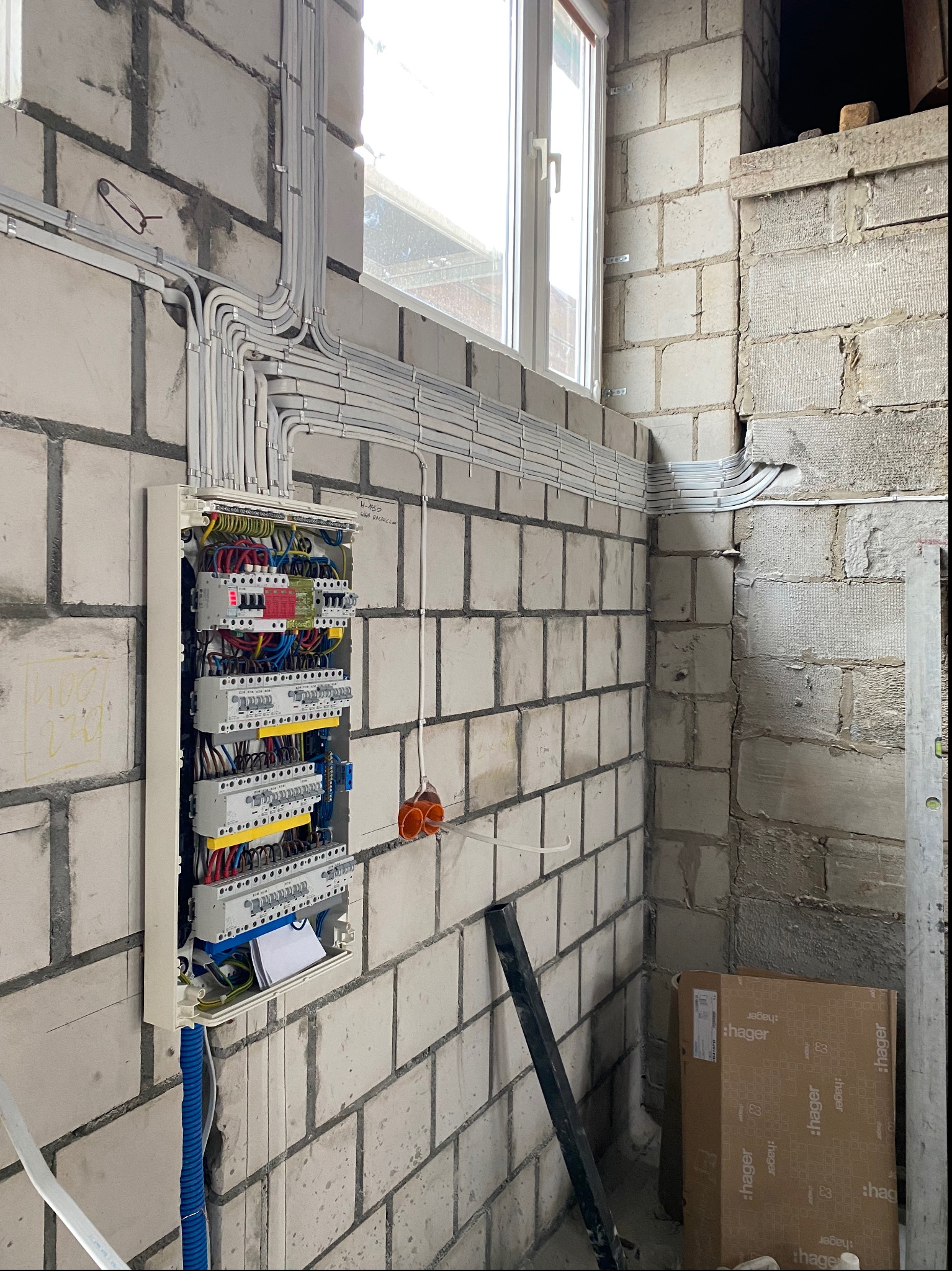 Rozdzielnica elektryczna z licznymi przewodami ułożonymi w peszlach na ścianie z betonu komórkowego, widoczne zabezpieczenia różnicowoprądowe i nadprądowe, puszki instalacyjne i kartonowe...