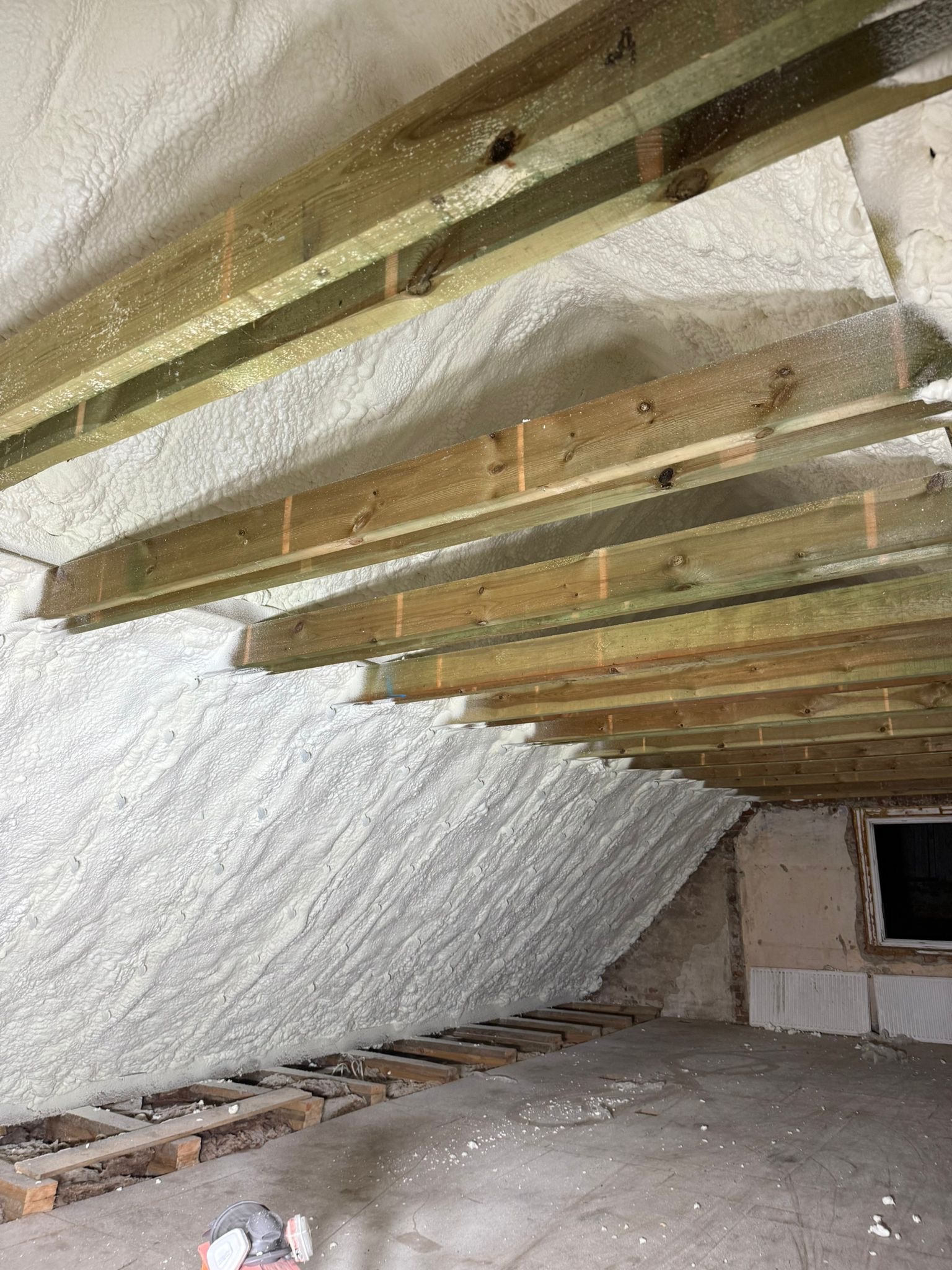 Poddasze po aplikacji pianki PUR w Grodzisku Mazowieckim. Widoczne drewniane elementy konstrukcyjne i równomierna warstwa izolacji. Charakterystyczna faktura pianki.