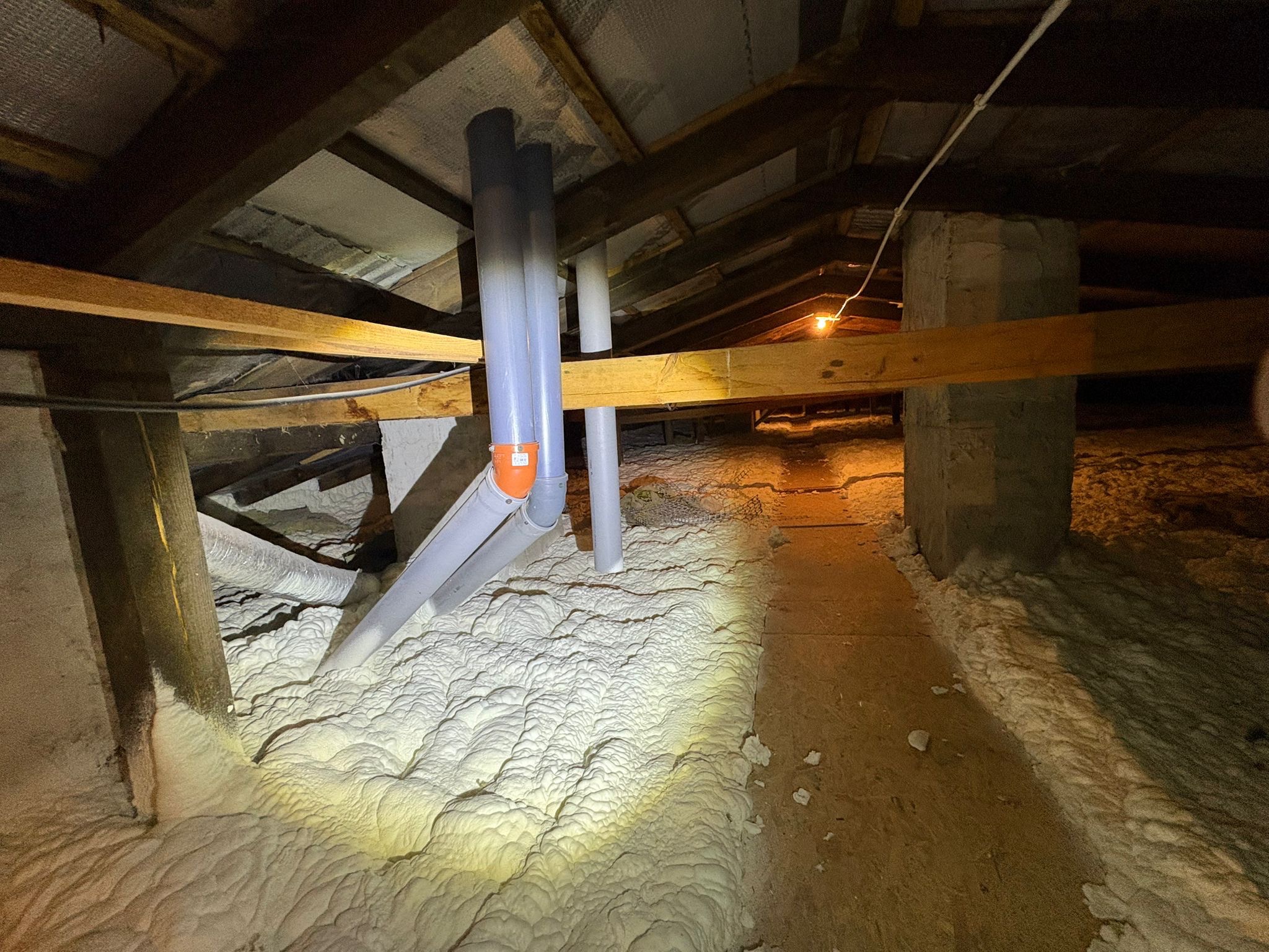 Poddasze z widoczną izolacją pianką PUR, rury wentylacyjne przechodzące przez warstwę izolacyjną, drewniana konstrukcja dachu. Oświetlenie punktowe.