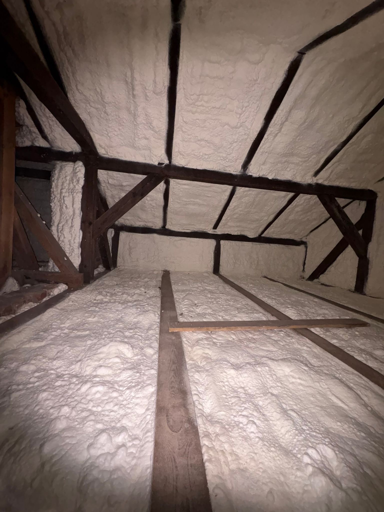 Poddasze z drewnianą konstrukcją pokryte grubą warstwą białej pianki izolacyjnej, widok z dołu, ukazujący strukturę i dokładność aplikacji.