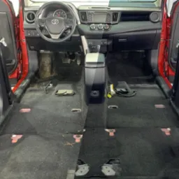 Wnętrze czerwonego samochodu przed i po praniu tapicerki podłogowej, widoczna wyraźna różnica w czystości dywaników po stronie prawej.