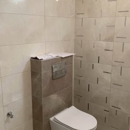 Przedsiębiorstwo Handlowo-Usługowe Patryk Milewski - Wisząca toaleta z zabudowanym stelażem, wykończona płytkami imitującymi marmur, na stelażu leżą plany łazienki, na ścianach płytki z geometrycznym wzorem.