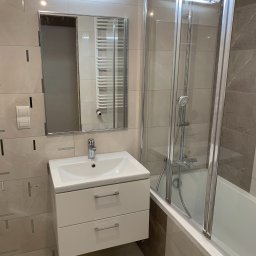 Przedsiębiorstwo Handlowo-Usługowe Patryk Milewski - Nowoczesna łazienka z beżowymi i brązowymi płytkami, białą szafką pod umywalką z szufladami i kabiną prysznicową z elementami chromowanymi.