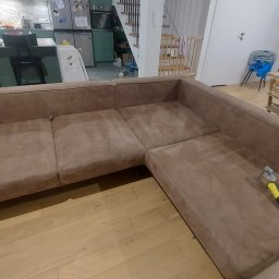 KlinOl - Pranie narożnika z mikrofibry w Warszawie za pomocą odkurzacza piorącego z żółtą końcówką; widok na salon z kuchnią w tle.