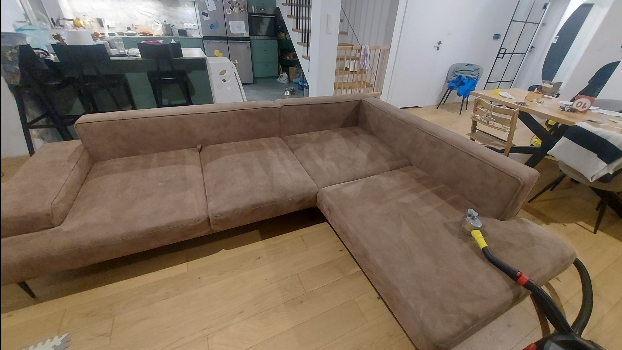 Pranie narożnika z mikrofibry w Warszawie za pomocą odkurzacza piorącego z żółtą końcówką; widok na salon z kuchnią w tle.