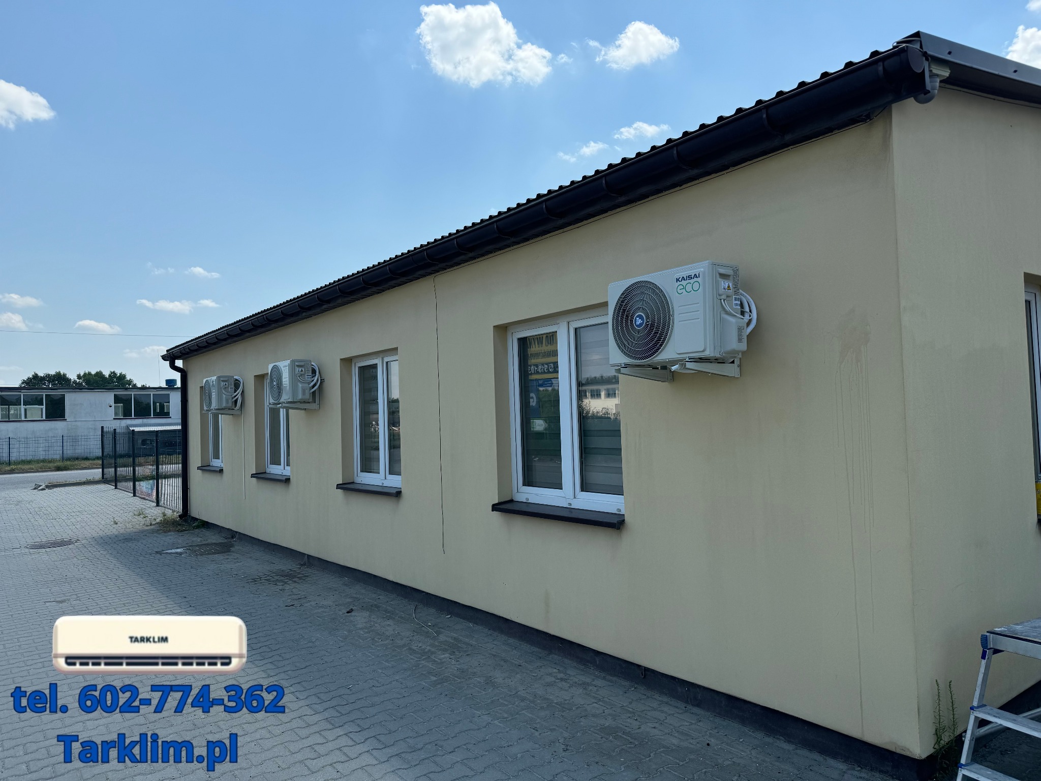 Fasada budynku z zamontowanymi klimatyzatorami Kaisai Eco, widoczne jednostki zewnętrzne, błękitne niebo i logo firmy TARKILM z numerem telefonu i adresem strony internetowej nałożone na zdjęcie.