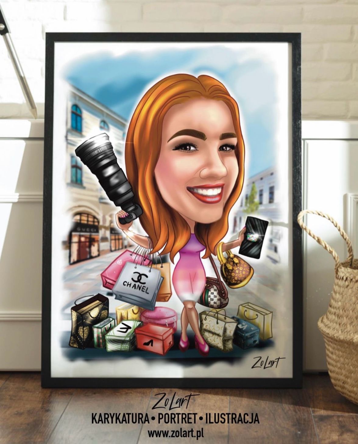 Oprawiony w ramę portret-karykatura uśmiechniętej kobiety z rudymi włosami, trzymającej aparat fotograficzny i telefon, otoczonej torbami na zakupy znanych marek, na tle miejskiej ulicy.