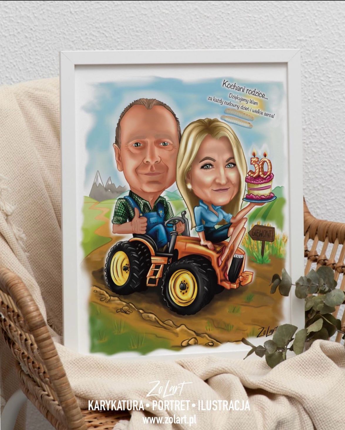 Oprawiona karykatura pary na pomarańczowym traktorze, z tortem urodzinowym z numerem 50, na tle górskiego krajobrazu, umieszczona na fotelu z wikliny.