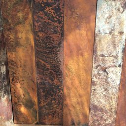 Daniel Leigna - Rdzewiejące, pionowe metalowe panele z wyraźną teksturą i zróżnicowaną kolorystyką odcieni brązu, pomarańczy i szarości, ukazujące proces korozji