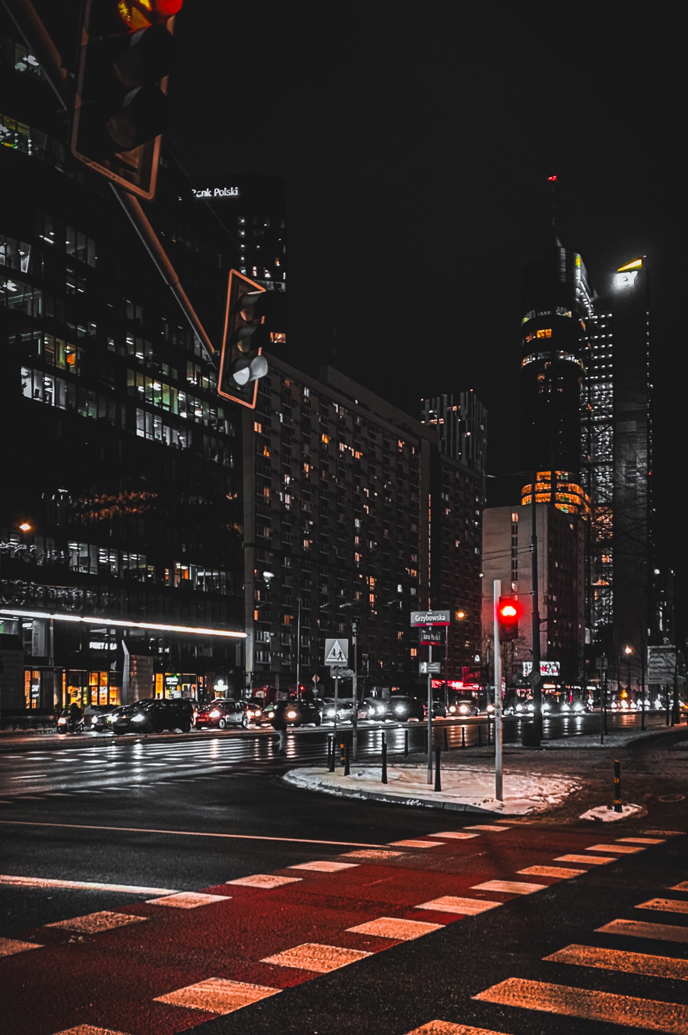 Nocny widok na skrzyżowanie ulic w mieście, z wieżowcami w tle i światłami sygnalizacji świetlnej.