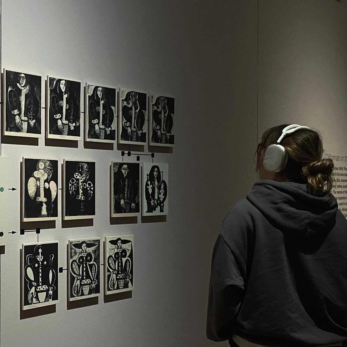 Osoba w słuchawkach ogląda czarno-białe obrazy na ścianie galerii sztuki, z widocznymi połączeniami między nimi.