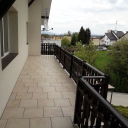 Usługi Remontowo-Wykończeniowe Paweł Czyrnek - Beżowe płytki na balkonie z drewnianą balustradą i widokiem na okolicę, antena satelitarna na ścianie budynku.