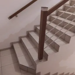 Klatka schodowa wyłożona jasnymi płytkami z brązową drewnianą balustradą z metalowymi poprzeczkami, widok z dołu, Polanica-Zdrój.