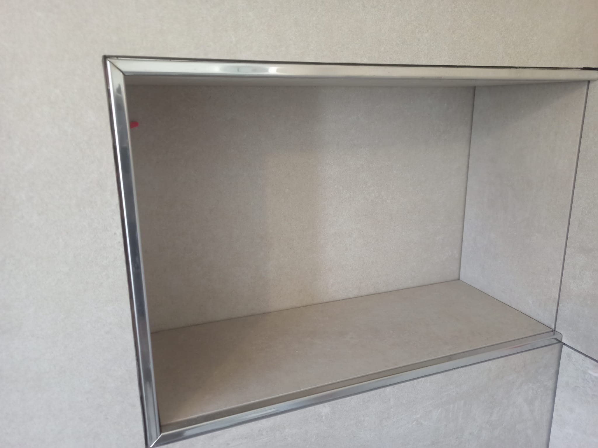 Wnęka w łazience wyłożona jasnymi płytkami ceramicznymi, obramowana metalową listwą, widok z bliska.