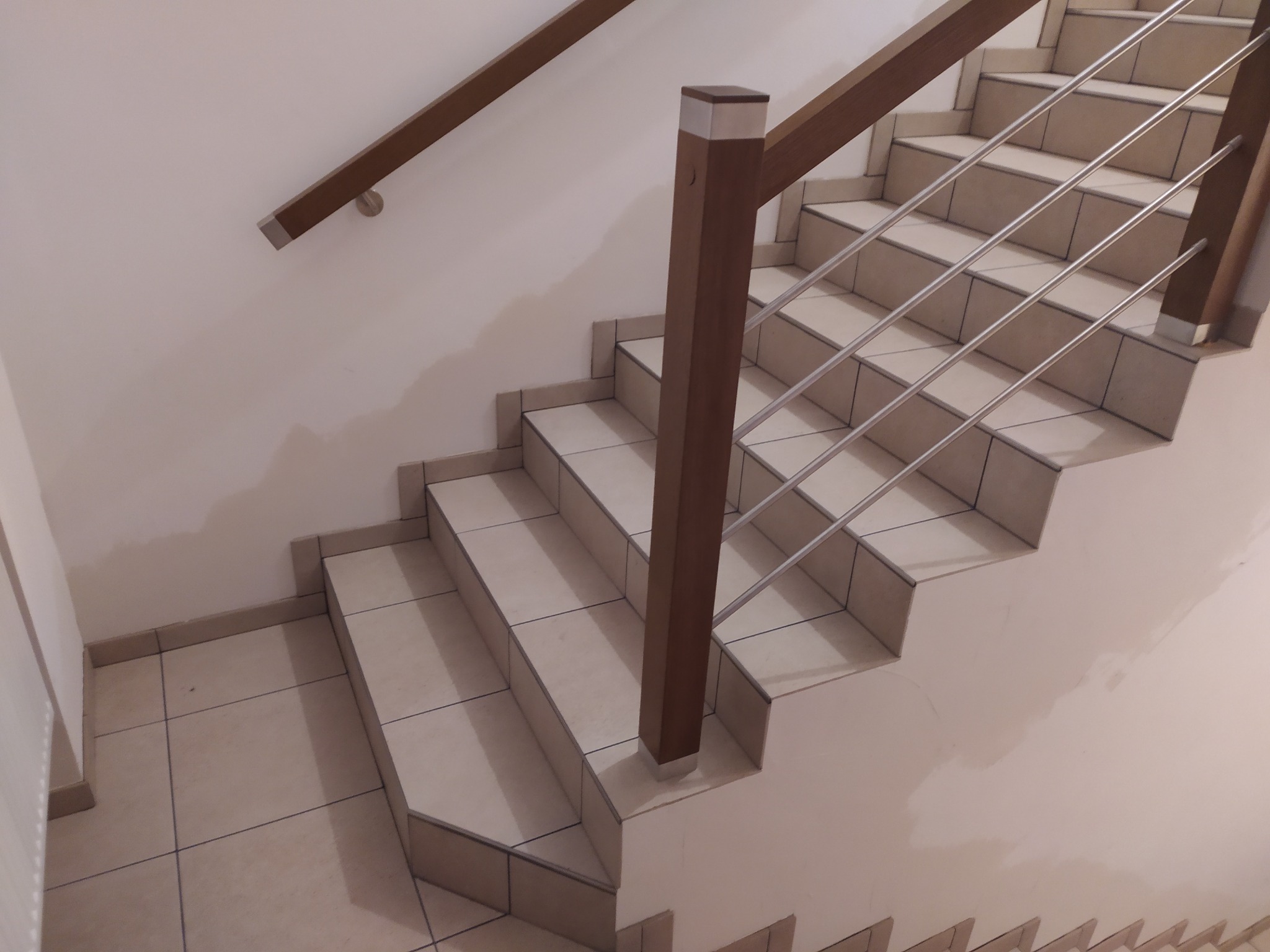 Klatka schodowa wyłożona jasnymi płytkami z brązową drewnianą balustradą z metalowymi poprzeczkami, widok z dołu, Polanica-Zdrój.