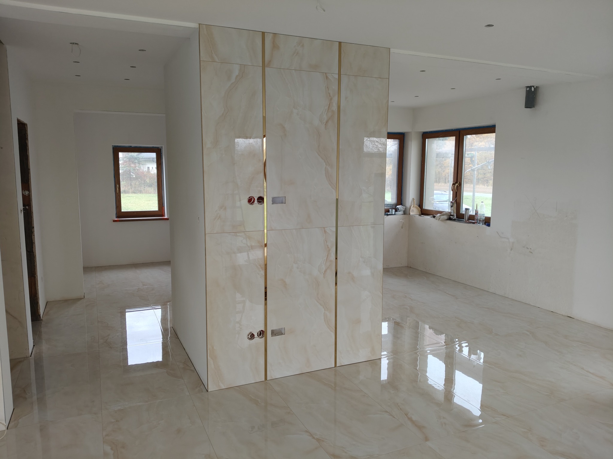 Wykończona podłoga i ściana z płytek imitujących marmur, z widocznymi gniazdkami elektrycznymi. Jasne wnętrze w trakcie prac wykończeniowych.