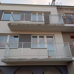 Kam-Weld - Dwa balkony z prostymi, metalowymi balustradami w budynku o szarej i białej elewacji, widok z dołu na tle pochmurnego nieba.