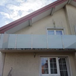 Kam-Weld - Zewnętrzna balustrada balkonowa ze szkła matowego i stali nierdzewnej, zamontowana na elewacji budynku o beżowej barwie z czerwonym dachem i ceglanym kominem.