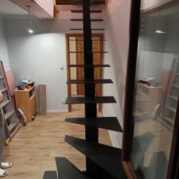 Kam-Weld - Czarne schody metalowe bez balustrady, zamontowane w surowym wnętrzu, widoczne narzędzia i materiały budowlane.