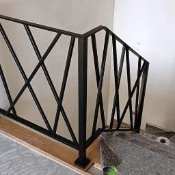 Kam-Weld - Nowoczesna, czarna balustrada metalowa o geometrycznym wzorze na schodach w trakcie montażu, zabezpieczonych folią ochronną.