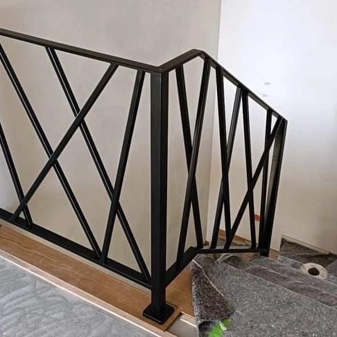 Nowoczesna, czarna balustrada metalowa o geometrycznym wzorze na schodach w trakcie montażu, zabezpieczonych folią ochronną.