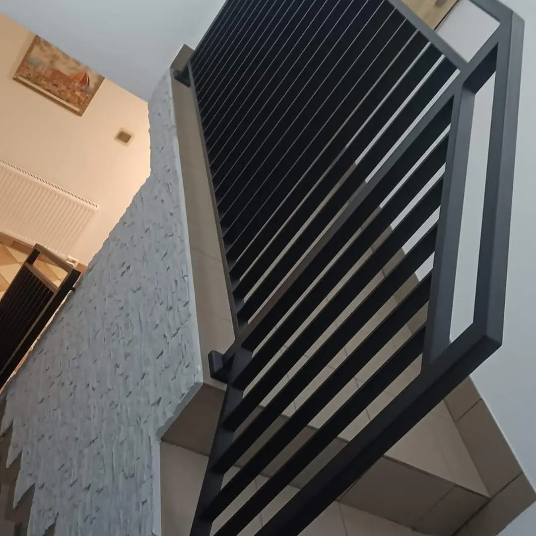 Nowoczesna, czarna balustrada metalowa z poziomymi szczeblami, zamontowana przy schodach z okładziną z kamienia dekoracyjnego; widok od dołu.
