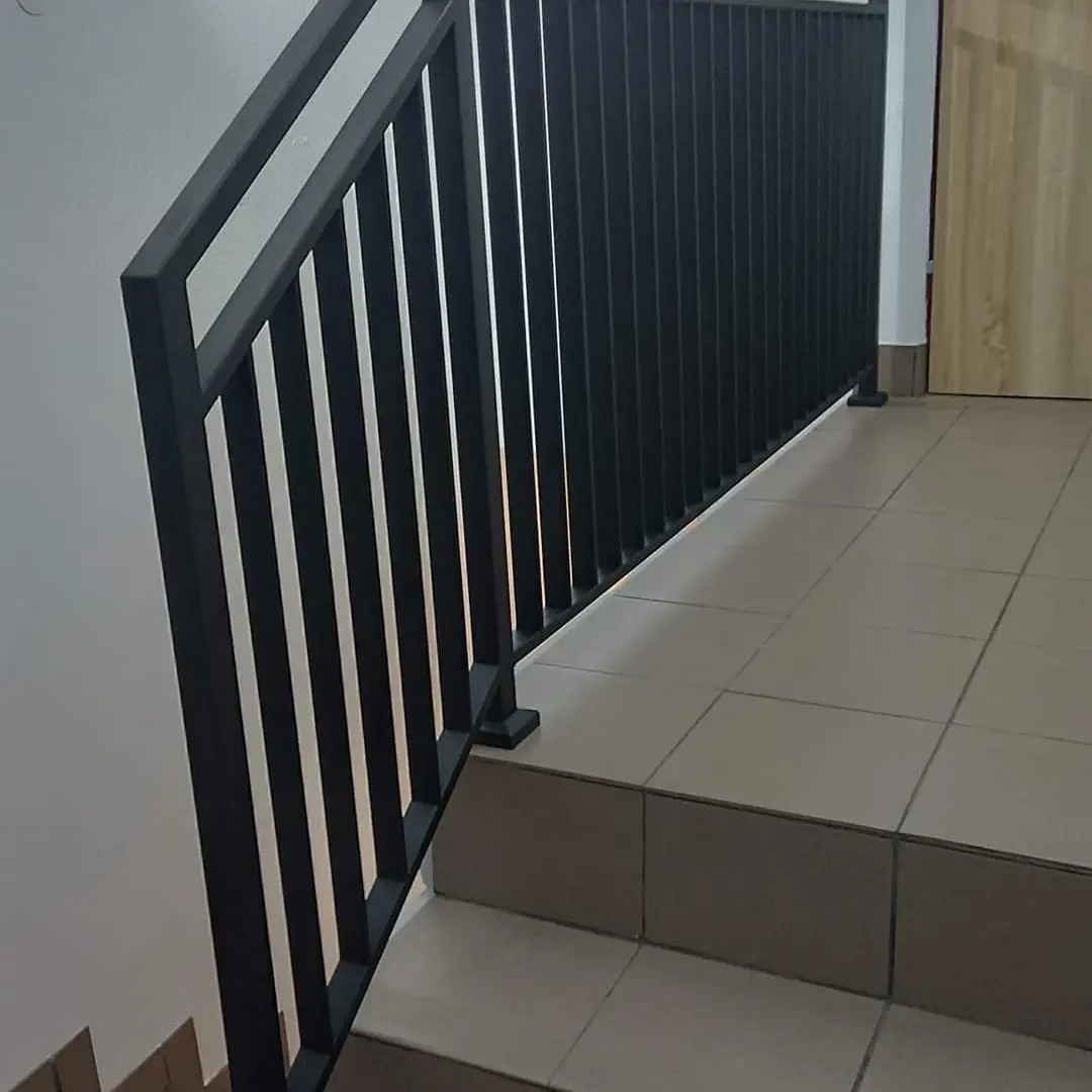 Czarne, metalowe schody z prostą balustradą z pionowych prętów, widok z dołu schodów wewnątrz budynku.