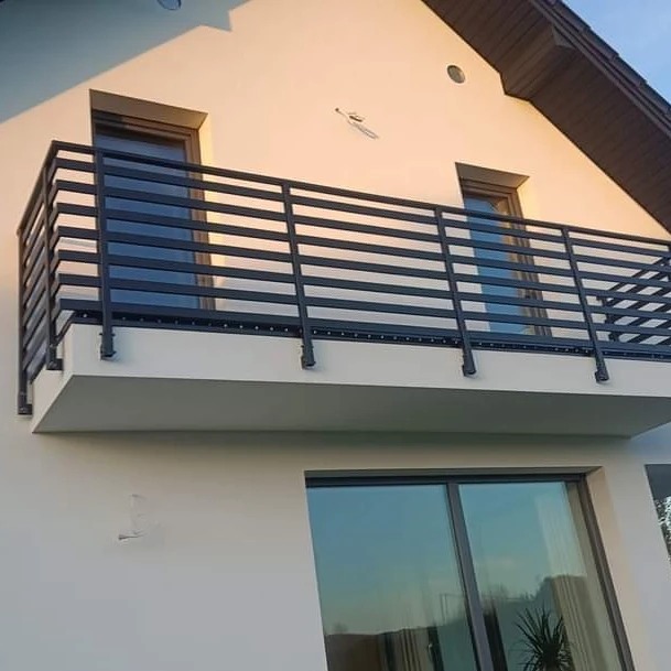 Nowoczesna, pozioma, czarna barierka balkonowa z metalowych profili zamontowana na jasnym budynku z dwoma oknami, widok z dołu.
