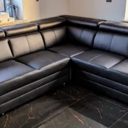 Czarny, skórzany narożnik modułowy z zagłówkami, ustawiony na podłodze z ciemnego marmuru z pomarańczowymi żyłami, widok z niskiej perspektywy.