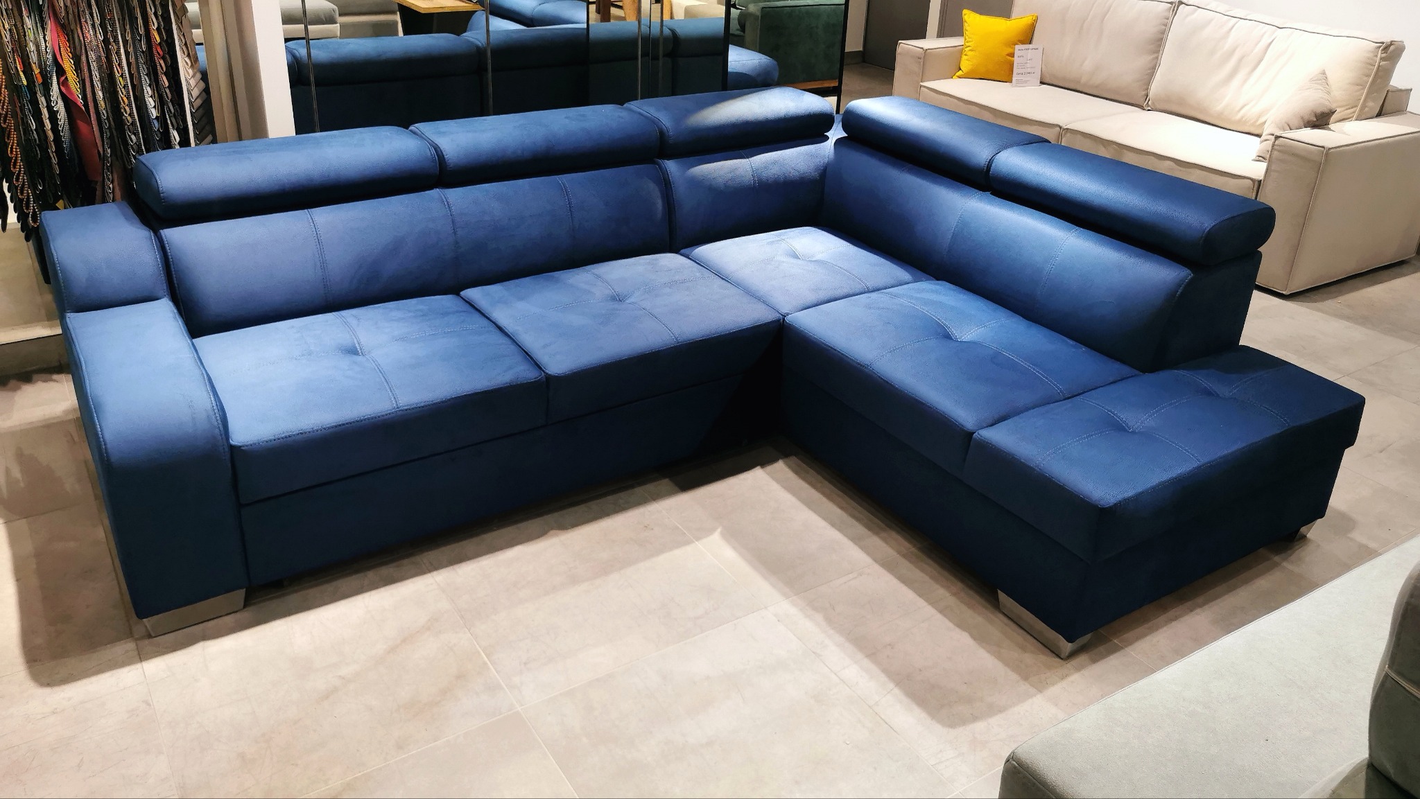 Narożnik tapicerowany w odcieniach niebieskiego z regulowanymi zagłówkami, widoczny w salonie meblowym na tle innych sof.