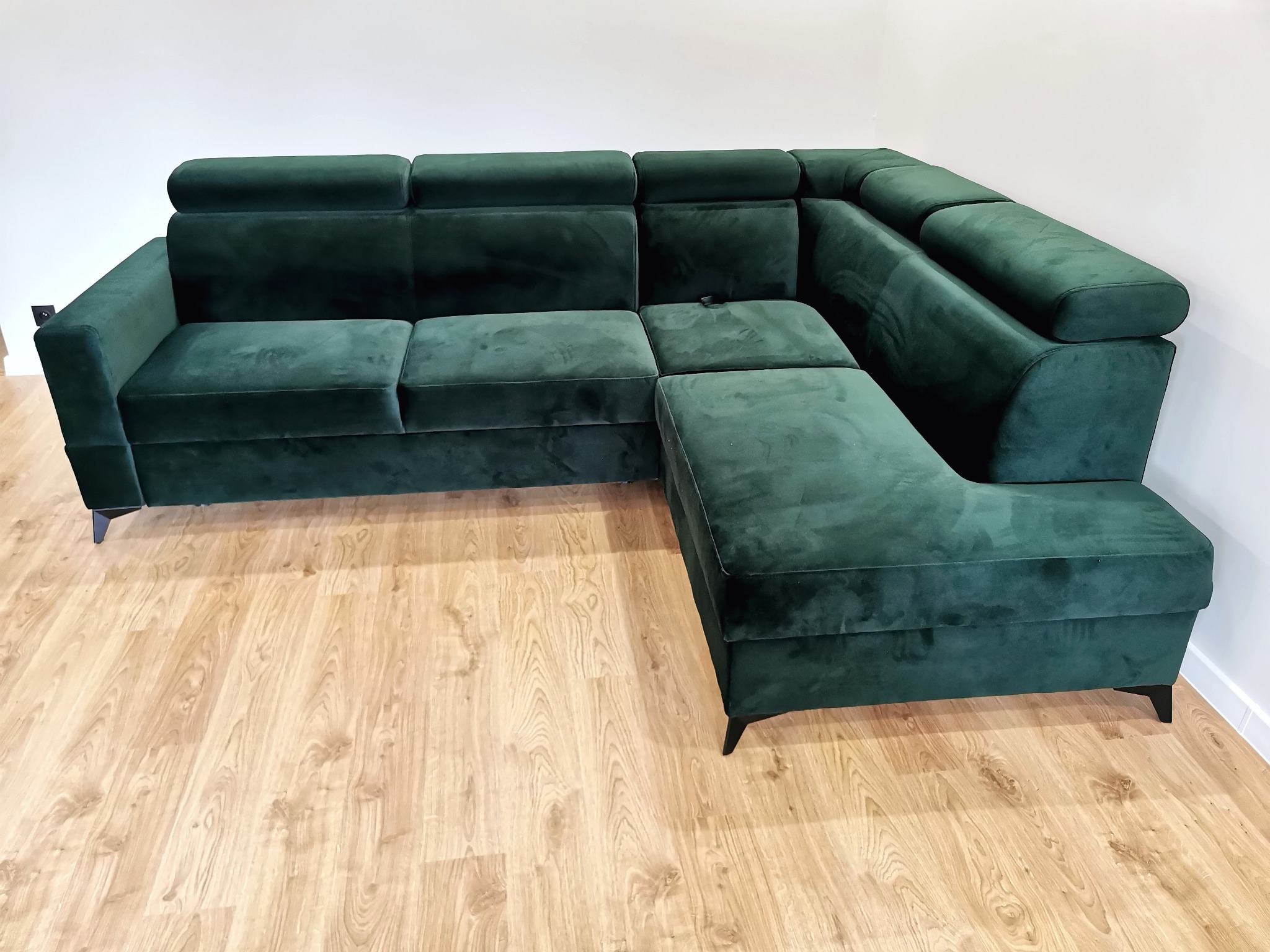 Szmaragdowa, welurowa narożna sofa z regulowanymi zagłówkami, ustawiona na parkiecie w jasnym wnętrzu w Kalwarii Zebrzydowskiej.