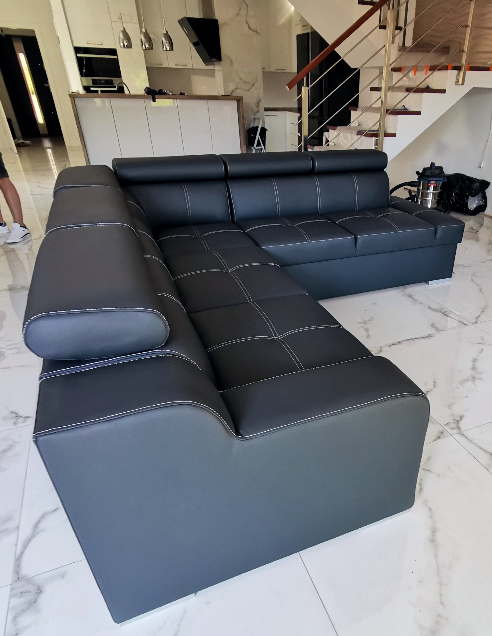 Czarny narożnik z jasnymi przeszyciami w nowoczesnym salonie z marmurową podłogą i schodami.