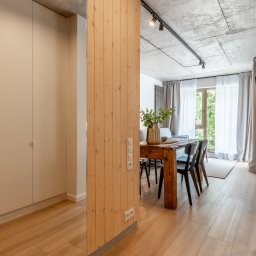 Karkonoskie Sny Marta Majkowska - Nowoczesne wnętrze jadalni z drewnianym stołem, czarnymi krzesłami i betonowym sufitem z oświetleniem punktowym, oddzielone drewnianą ścianką działową z gniazdkami elektrycznymi.