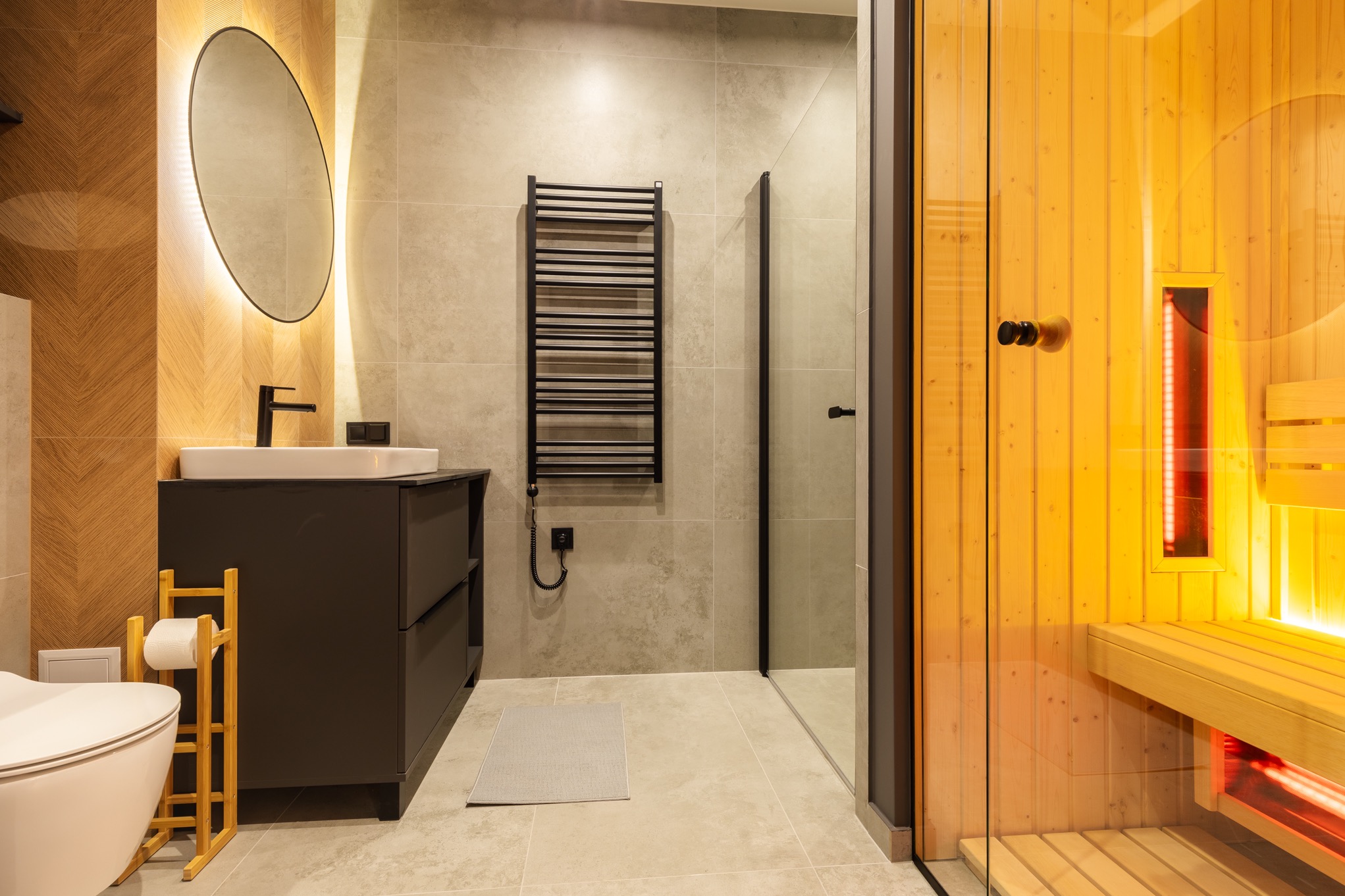 Nowoczesna łazienka z kabiną prysznicową i sauną infrared, szara glazura, czarna armatura i grzejnik drabinkowy.