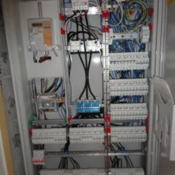 Rozdzielnia elektryczna z licznikiem, zabezpieczeniami i okablowaniem, widok z bliska na elementy wewnątrz szafy, szyny montażowe, przewody w różnych kolorach.