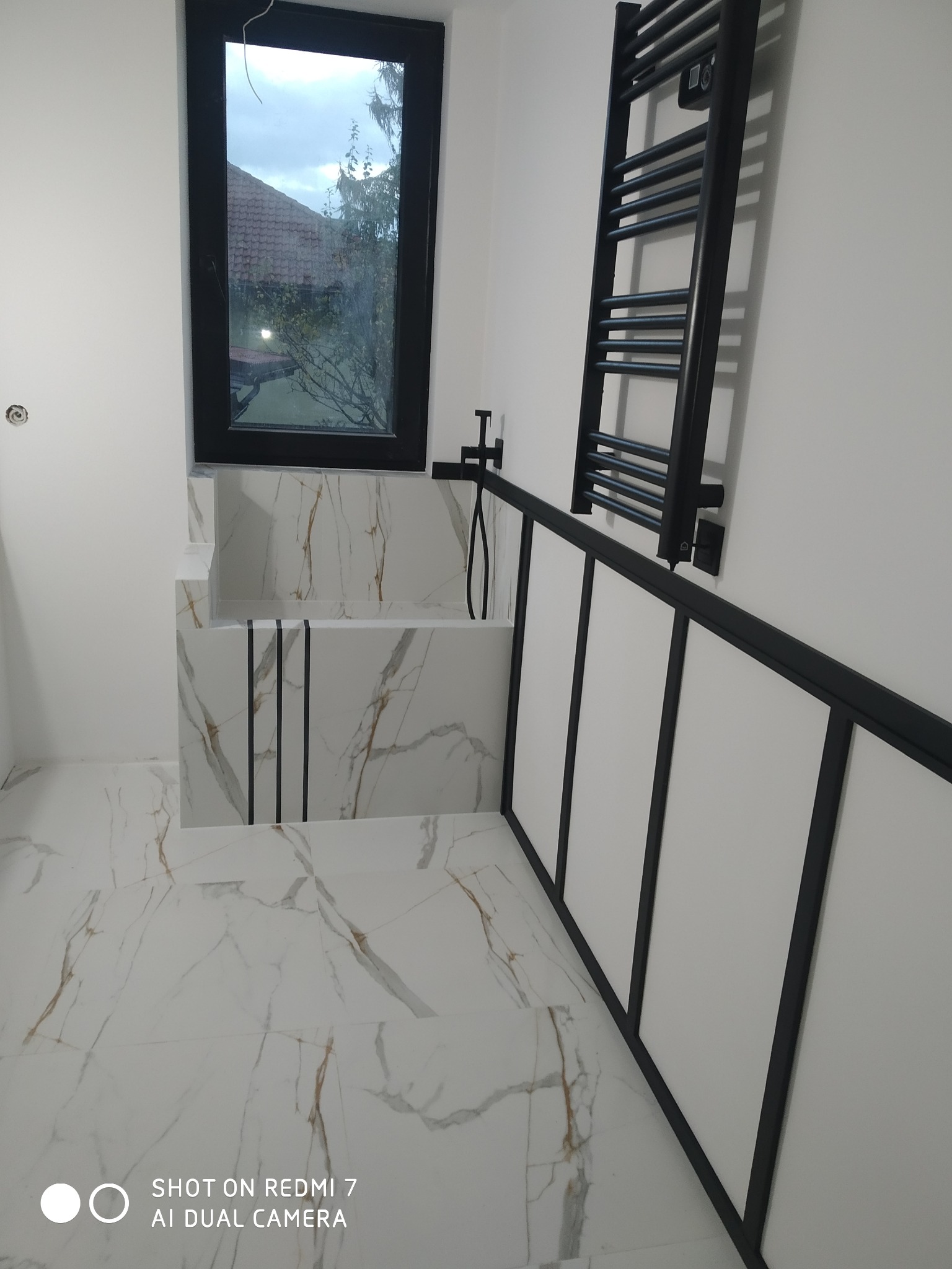 Nowoczesna łazienka z marmurową wanną, czarną armaturą i grzejnikiem drabinkowym, widok z góry z perspektywy podłogi.