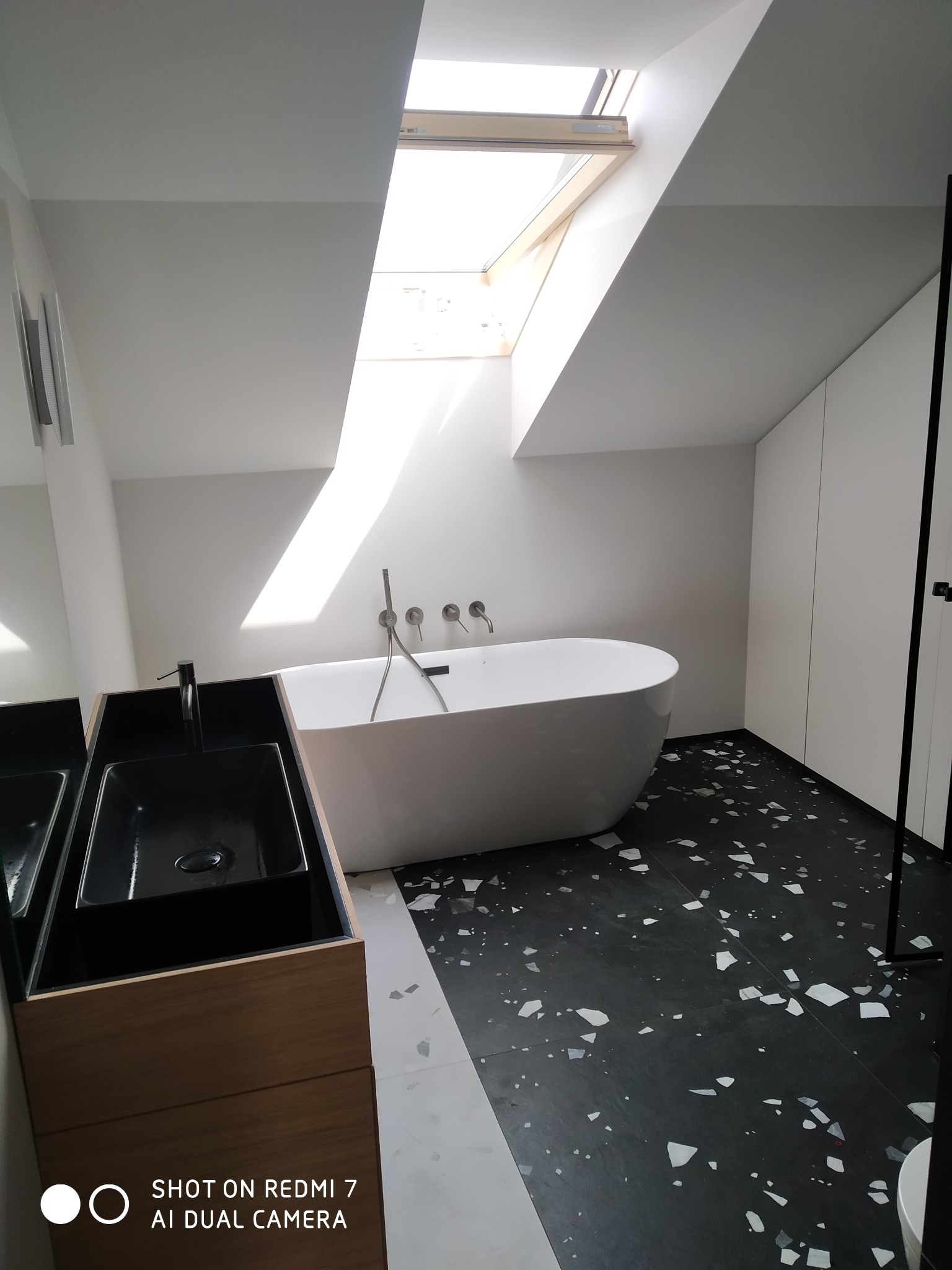 Nowoczesna łazienka na poddaszu z oknem dachowym, wolnostojąca wanna, czarna umywalka nablatowa i podłoga w stylu lastryko.