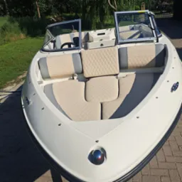 Wnętrze łodzi motorowej z jasną, pikowaną tapicerką w odcieniach beżu i szarości, widok z przodu na siedzenia i kokpit.