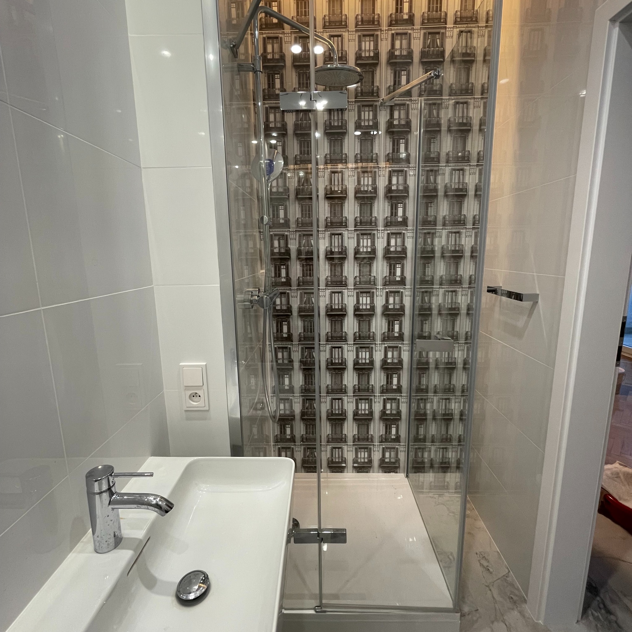 Nowoczesna łazienka z kabiną prysznicową z szybą z motywem kamienicy, białą umywalką i chromowaną baterią, wykończona jasnymi płytkami.