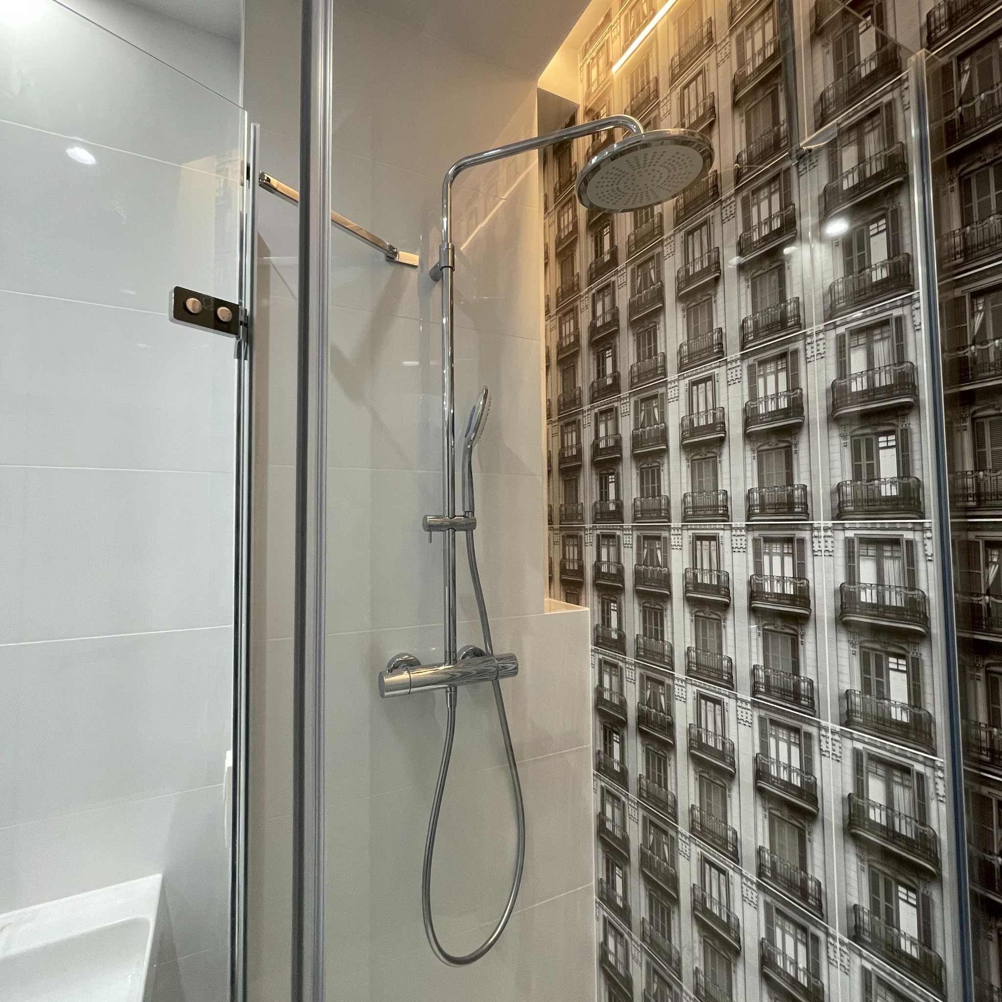 Kabina prysznicowa z deszczownicą i baterią termostatyczną na tle ściany z fototapetą przedstawiającą kamienicę.