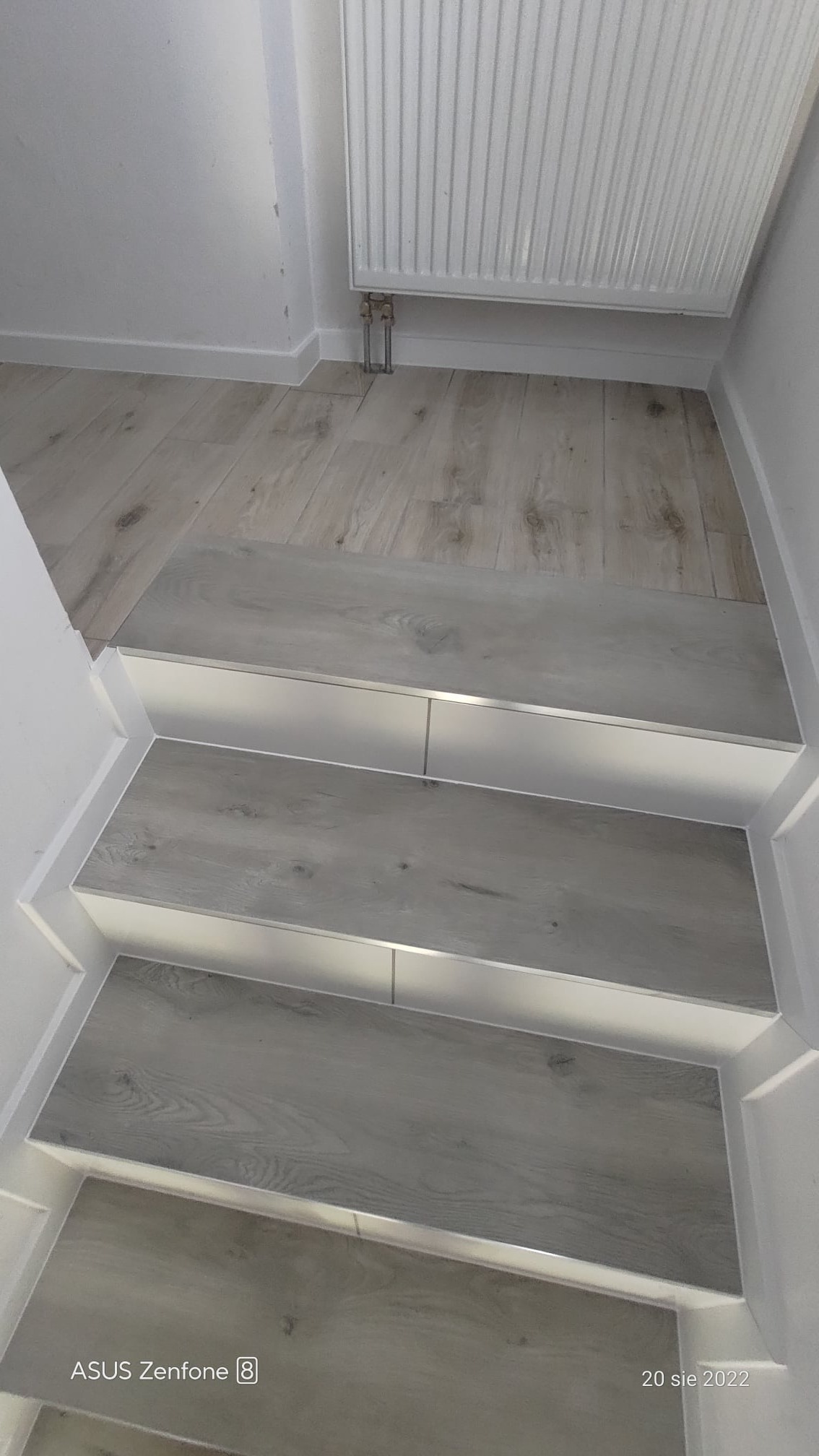 Schody wykończone panelami imitującymi drewno w Garbatce-Letnisko, z widoczną listwą wykończeniową i grzejnikiem na podłodze.