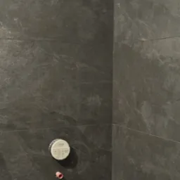 Szare płytki imitujące kamień na ścianie łazienki, widoczne przyłącza Grohe i rurka, etap prac wykończeniowych.