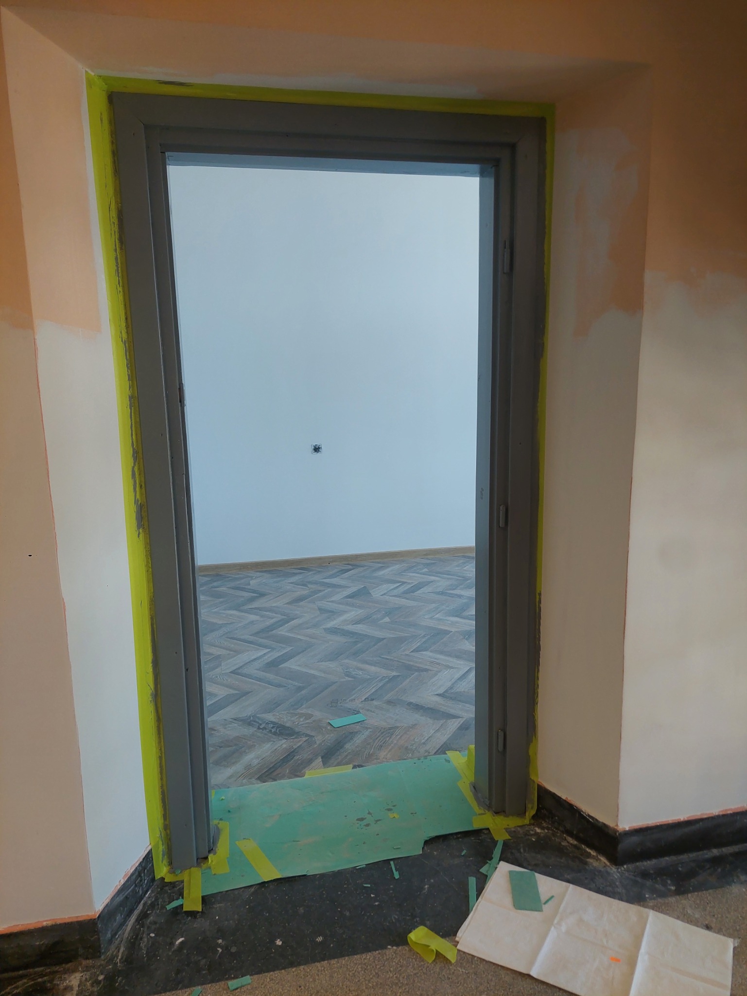 Przygotowanie do malowania futryny drzwiowej z zabezpieczeniem taśmą malarską i folią ochronną w Zabrzu. Widoczne ślady szpachlowania ścian.