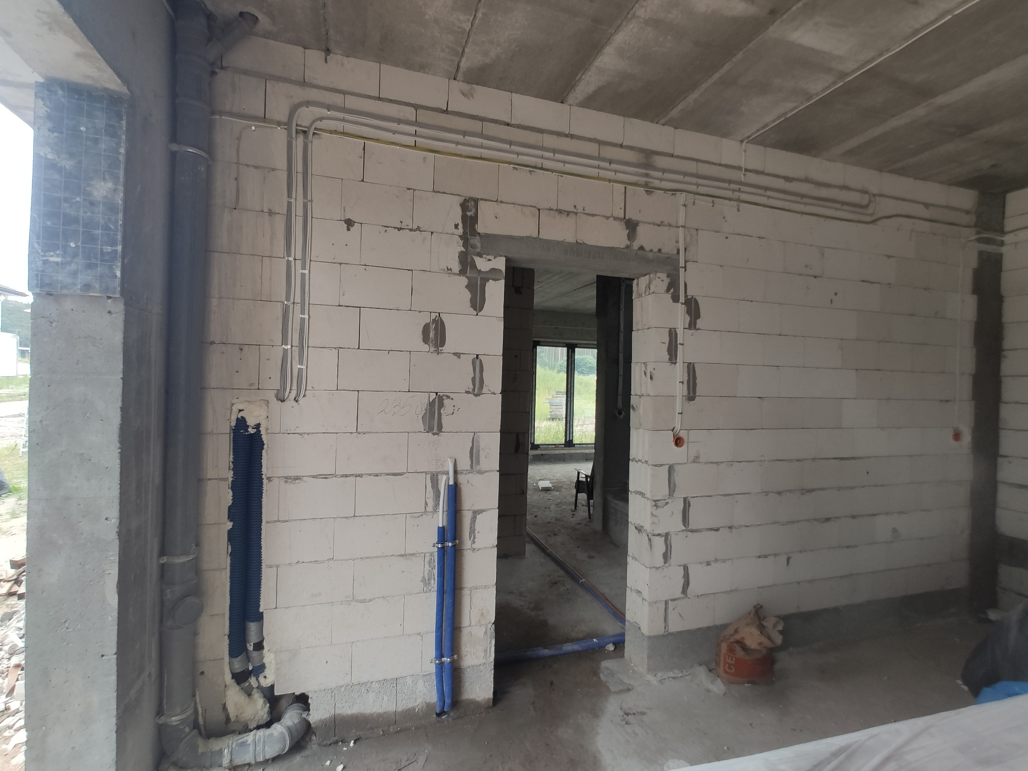 Surowy stan wnętrza budynku w trakcie budowy, widoczne przewody elektryczne i rury instalacyjne poprowadzone po ścianach z betonu komórkowego i pod sufitem. Na ścianach zamontowane puszki...