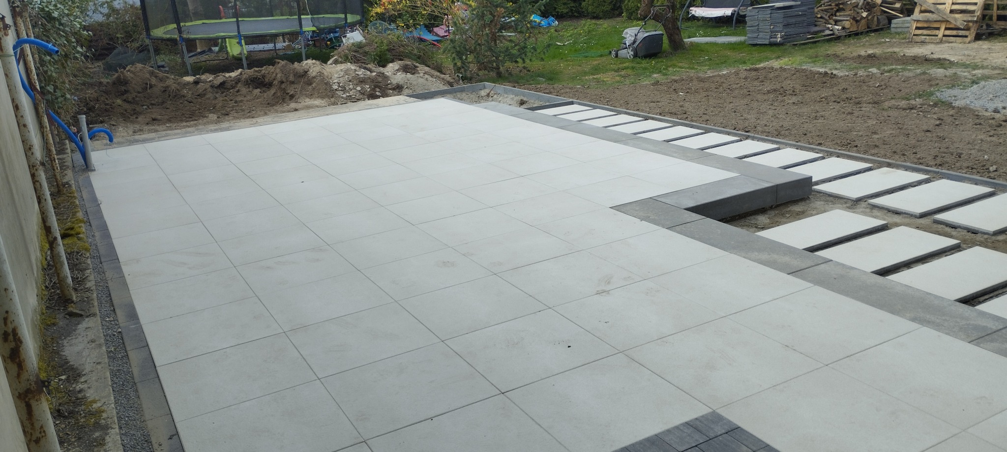 Jasna, nowo ułożona nawierzchnia z płyt betonowych w ogrodzie, z widocznymi elementami obrzeży i przygotowanym podłożem pod dalsze prace.