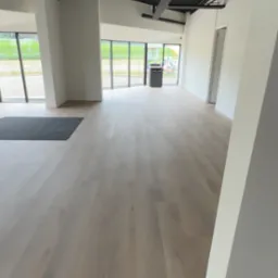 Jasne, drewnopodobne panele podłogowe w przestronnym, nowoczesnym biurze z czarnym sufitem podwieszanym i klimatyzacją kasetonową.