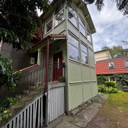 White Crow Usługi Remontowo-Budowlane Jacek Gdaniec - Odnowiona elewacja domu z drewnianą dobudówką w odcieniach zieleni, z widocznymi schodami wejściowymi i elementami dekoracyjnymi.