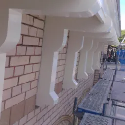 Elewacja budynku z cegły po malowaniu elementów dekoracyjnych na biało, widoczne rusztowania. Detal wykończenia elewacji.