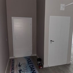 White Crow Usługi Remontowo-Budowlane Jacek Gdaniec - Świeżo pomalowane wnętrze z dwoma białymi drzwiami i puszkami farby Dulux. Na podłodze mata z logo studia tańca na rurze.