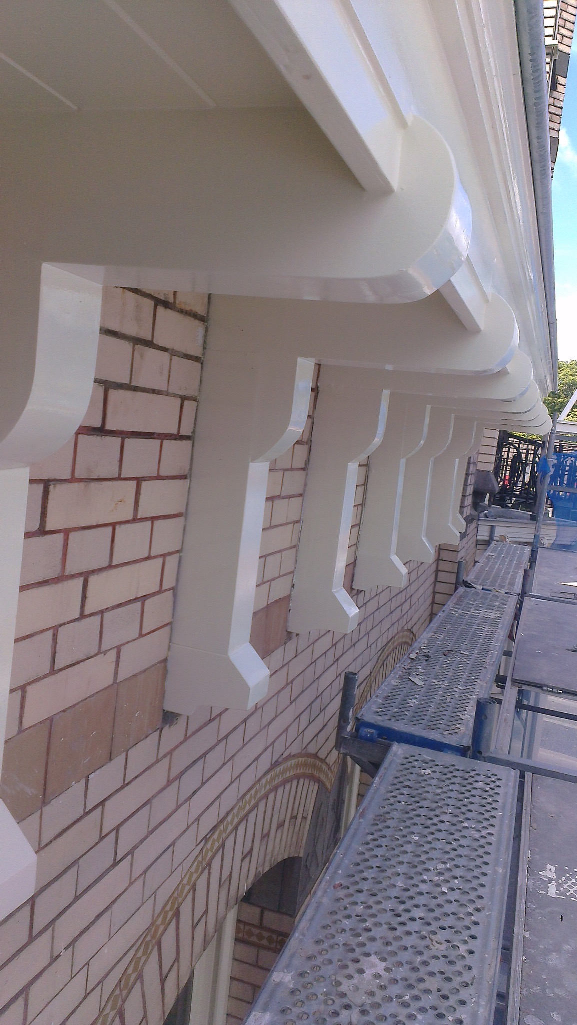 Elewacja budynku z cegły po malowaniu elementów dekoracyjnych na biało, widoczne rusztowania. Detal wykończenia elewacji.